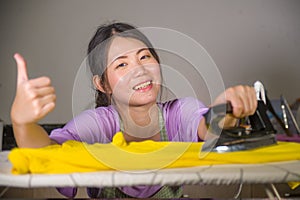 Young pretty and happy Asian Korean woman using iron at home kitchen ironing clothes smiling cheerful and carefree enjoying domest