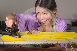 Young pretty and happy Asian Korean woman using iron at home kitchen ironing clothes smiling cheerful and carefree enjoying domest