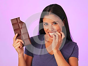 Young pretty and happy hispanic woman holding chocolate bar with teeth bite smiling in sugar and sweet addiction concept