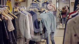 Young pretty happy woman taking photos of herself with a dress on her smartpohone camera in a clothing store