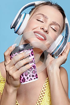 Young pretty happy woman in yellow dress drinking coffee and listening to music in headphones