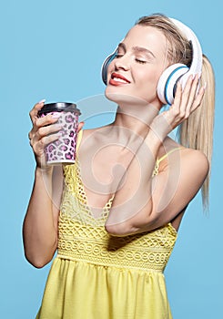 Young pretty happy woman in yellow dress drinking coffee and listening to music in headphones