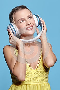 Young pretty happy woman in yellow dress listening to music in headphones