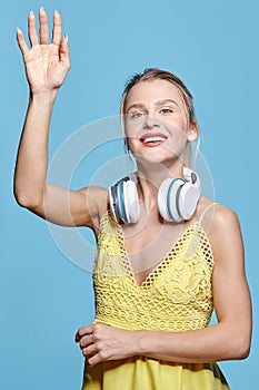 Young pretty happy woman in yellow dress listening to music in headphones on blue background