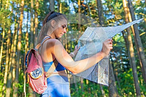 Young pretty hiker woman with backpack holding map in summer forest. Active lifestyle concept