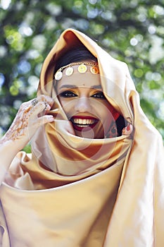 Young pretty indian girl in jewelry and veil posing cheerful happy smiling in green park, lifestyle people concept