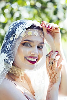 Young pretty indian girl in jewelry and veil posing cheerful happy smiling in green park, lifestyle people concept