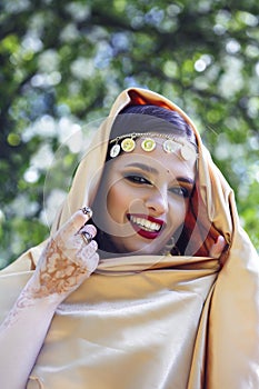 Young pretty indian girl in jewelry and veil posing cheerful happy smiling in green park, lifestyle people concept