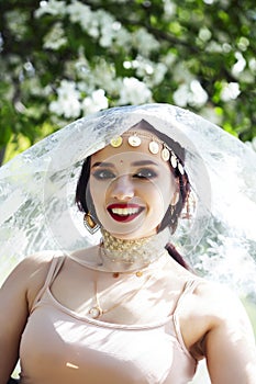 Young pretty indian girl in jewelry and veil posing cheerful happy smiling in green park, lifestyle people concept