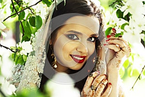 young pretty indian girl in jewelry and veil posing cheerful happy smiling in green park, lifestyle people concept