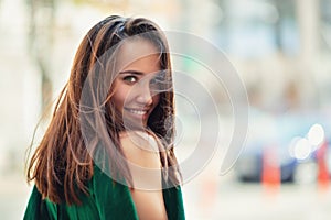 Young pretty likable cheerful woman posing summer city outdoor. Beautiful self-confident girl dressed in emerald-colored jumpsuit photo