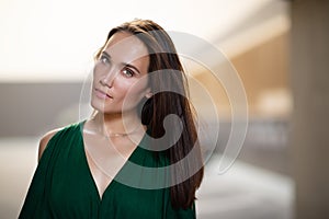 Young pretty likable cheerful woman posing summer city outdoor. Beautiful self-confident girl dressed in emerald-colored jumpsuit photo