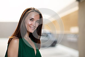 Young pretty likable cheerful woman posing summer city outdoor. Beautiful self-confident girl dressed in emerald-colored jumpsuit