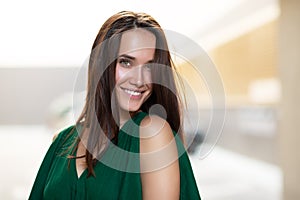 Young pretty likable cheerful woman posing summer city outdoor. Beautiful self-confident girl dressed in emerald-colored jumpsuit photo