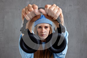 A young pretty long-haired DJ girl in a blue sweater and a funny blue hat holds black headphones in outstretched hands