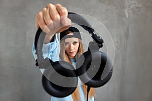 A young pretty long-haired DJ girl in a blue sweater and a funny blue hat holds black headphones in outstretched hands