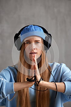 A young pretty long-haired DJ girl in a blue sweater, funny hat and headphones folded her hands in a prayerful