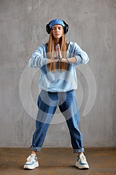 A young pretty long-haired DJ girl in a blue sweater, funny hat and headphones folded her hands in a prayerful