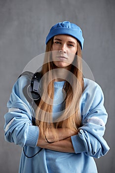 A young pretty long-haired girl in a blue sweater and a funny hat with black DJ headphones on her shoulder folded her