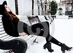 Young pretty modern hipster girl waiting on bench at winter snow park alone, lifestyle people concept