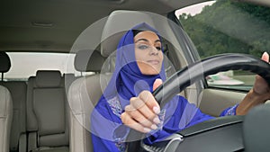 Young pretty muslim woman in hijab driving a car on the road, smiling