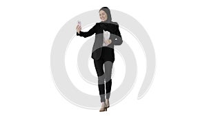 Young pretty muslim woman in hijab having video call on her phone as she walks on white background.