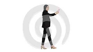 Young pretty muslim woman in hijab having video call on her phone as she walks on white background.