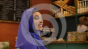 Young pretty muslim woman in hijab sitting in restaurant and smiling at camera