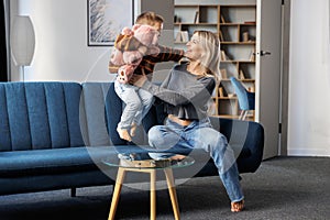 Young pretty pregnant woman having fun with her son at home. The boy happily jumps on the sofa