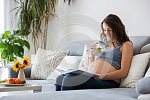 Young pretty pregnant woman reading book at home on the couch