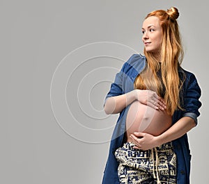 Young pretty red hair pregnant bump woman standing on a grey bac