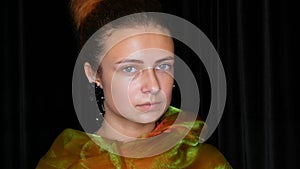 Young pretty red-haired teen girl in black earrings and a green scarf poses without makeup in model photo studio