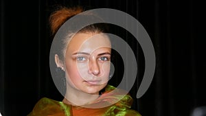 Young pretty red-haired teen girl in black earrings and a green scarf poses without makeup in model photo studio