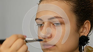Young pretty red-haired teenager girl applying concealer with special brush on her face