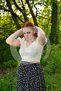 A young pretty redhead woman, hands on hair, in green nature