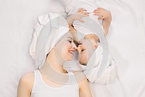 Young pretty relaxed woman mom and her cute little baby girl at home, with towels on heads after bath, lying on bed head