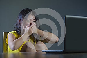 Young pretty shocked and surprised Asian Korean woman looking stressed at laptop computer feeling amazed and scared in cyber bully