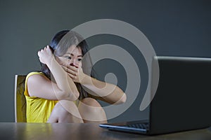 Young pretty shocked and surprised Asian Korean woman looking stressed at laptop computer feeling amazed and scared in cyber bully