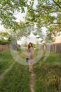 A young pretty slender girl walks along an abandoned rural road with a retro suitcase wrapping her hair fluttering