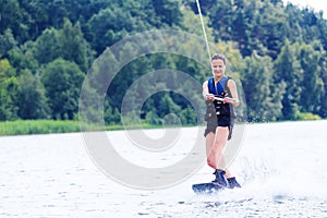 Young pretty slim brunette woman riding wakeboard on wave of motorboat in summer lake