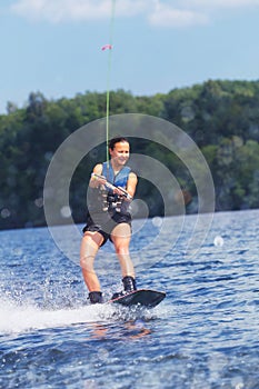 Young pretty slim brunette woman riding wakeboard on wave of motorboat in summer lake