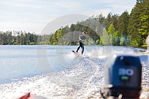 Young pretty slim brunette woman in wetsuit riding wakeboard on