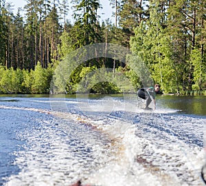 Young pretty slim brunette woman in wetsuit riding wakeboard on wave of motorboat