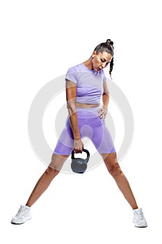 Young pretty slim woman in purple sportswear is doing exercises with a kettlebell. Energy, sports, health and movement. Isolated