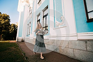 A young pretty smiling girl with blond hair, in a gray dress with a paper guide in her hands