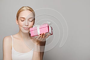 Young pretty smiling woman holding pink gift box and looking at camera on white background