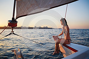 Young pretty smiling woman at luxury yacht in sea, looking forward, sunset evening time