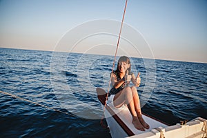 Young pretty smiling woman in striped shirt and white shorts at luxury yacht in sea, sunset