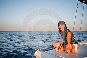 Young pretty smiling woman in striped shirt and white shorts at luxury yacht in sea, sunset