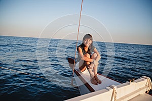 Young pretty smiling woman in striped shirt and white shorts at luxury yacht in sea, sunset